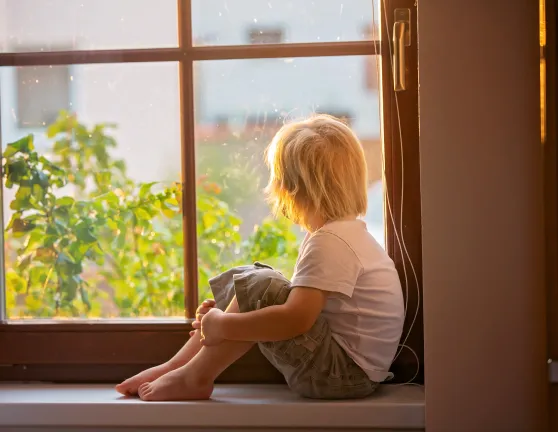 Niño pequeño mirando por la ventana dentro de su casa