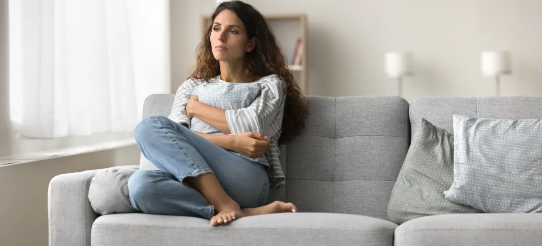 Mujer con expresión de tristeza sentada en el sofá de su casa